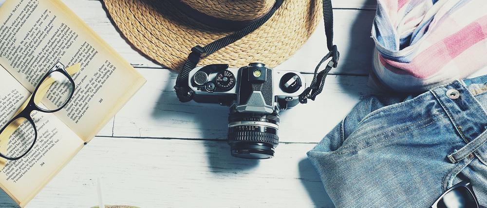 Painted floor boards with a camera, sun hat, open book, sunglasses and clothes.