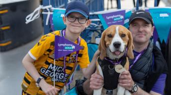 Man and boy holding Lymphoma Action flag with dog wearing a medal