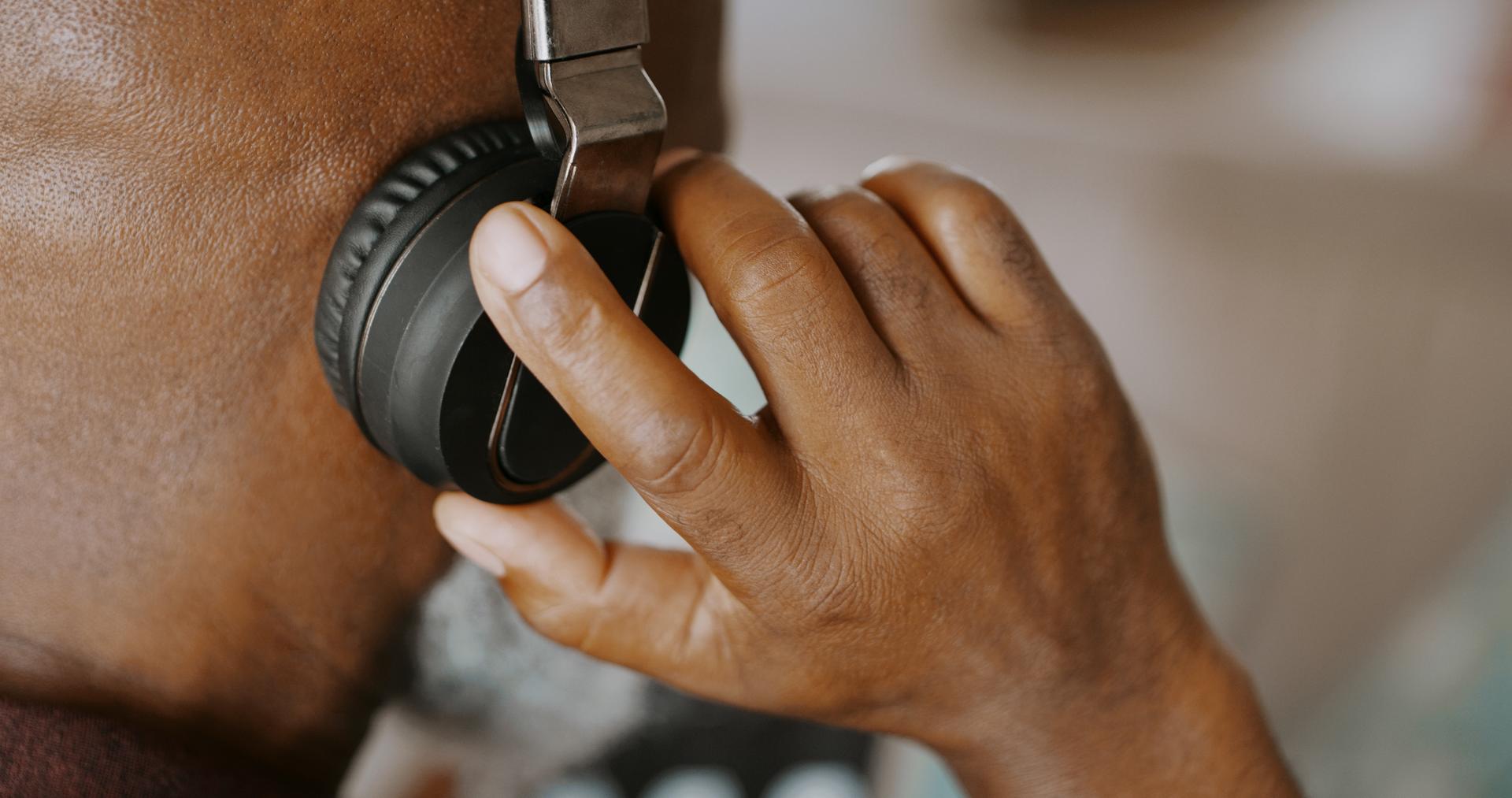 Person wearing headphones and their hand is on their ear.