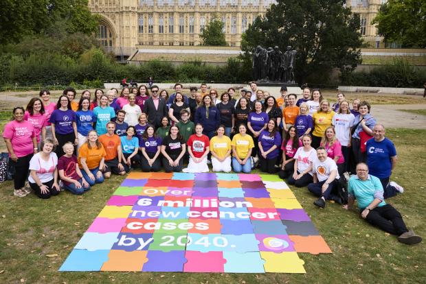 A large group of charity workers behind a large jigsaw with key cancer statistics printed on the pieces