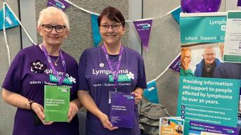 Two Lymphoma Action volunteers smiling at a stall of lymphoma information