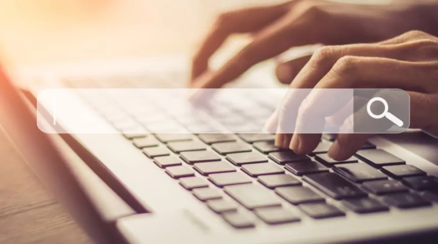 Hands typing on a laptop keyboard with a search bar over the top of the image