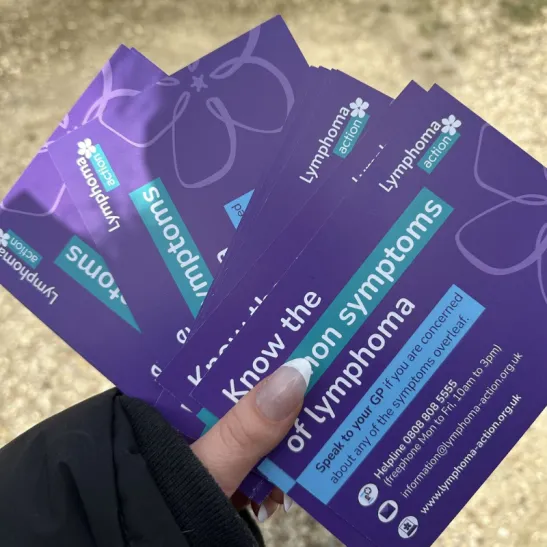Image shows a person's hand holding several purple lymphoma symptoms cards.