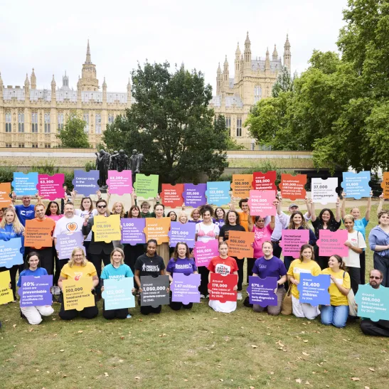 A large group of charity workers holding up jigsaw pieces with key cancer statistics printed on them