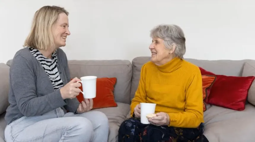 Two people sat on a sofa talking and holding a drink