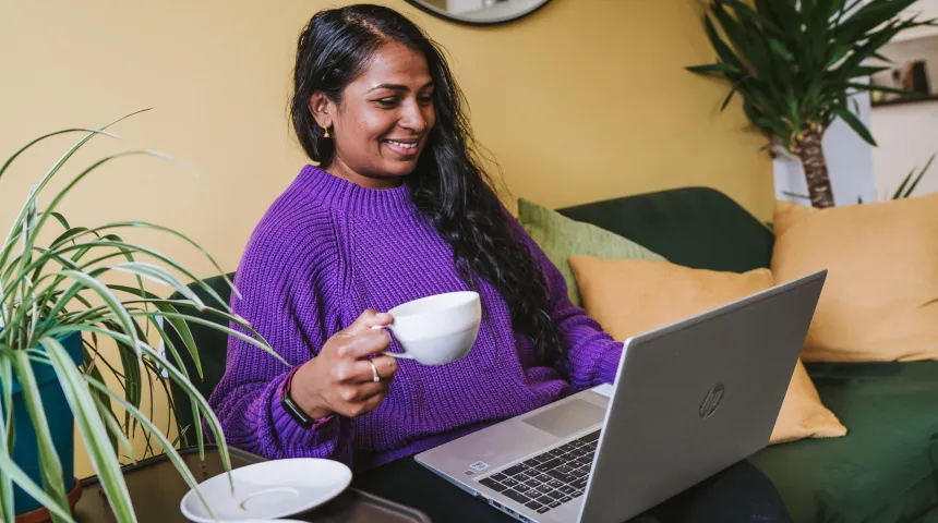 Person sat looking a laptop with cup in hand
