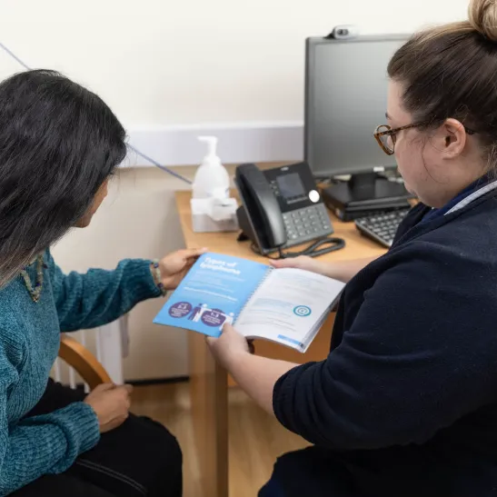 Clinical nurse specialist sitting with a patient in clinic with an information book