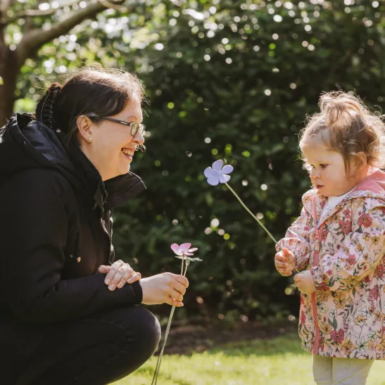 Mother and daughter standing opposite each other holding periwinkle flowers