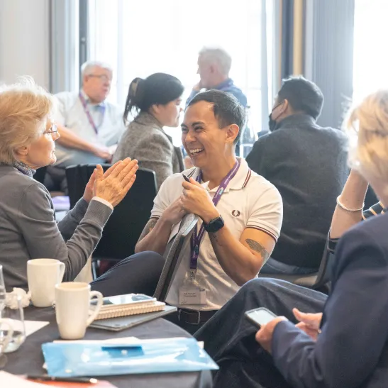 A group of people sat at a round table smiling and talking to one another