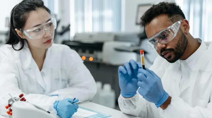 An image of a man and woman in lab coats looking at a test tube filled with a dark liquid