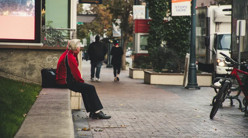 An image of a man sitting on the side of a wall in a city looking around and waiting