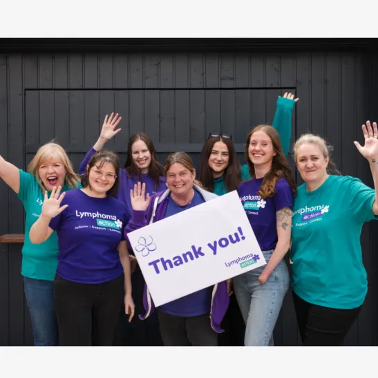 Seven members of the Lymphoma Action team are wearing branded t shirts and waving at the camera.  A team member at front centre is holding a sign that reads 'thank you'